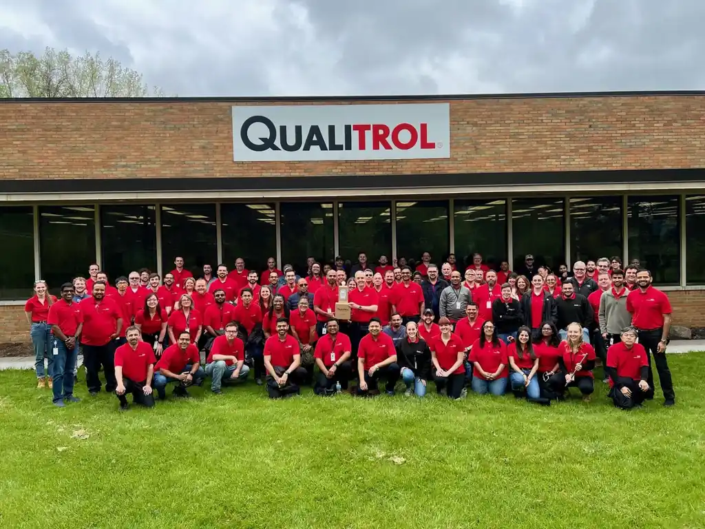 Large group of Qualitrol employees in red shirts gathered in front of company headquarters building
