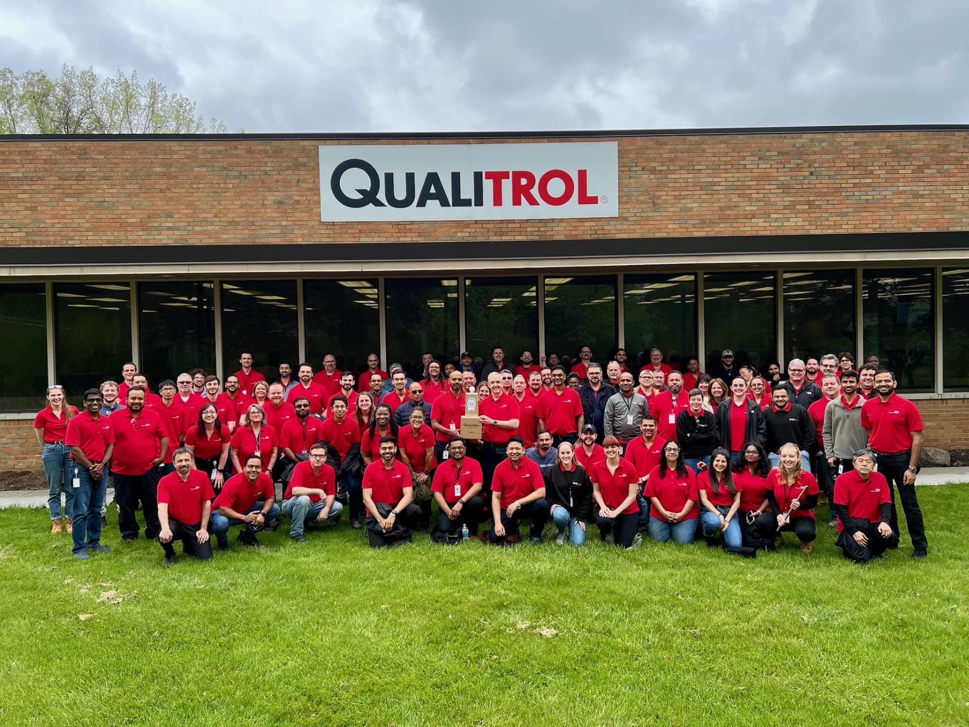 Large group of Qualitrol employees in red shirts gathered in front of company headquarters building